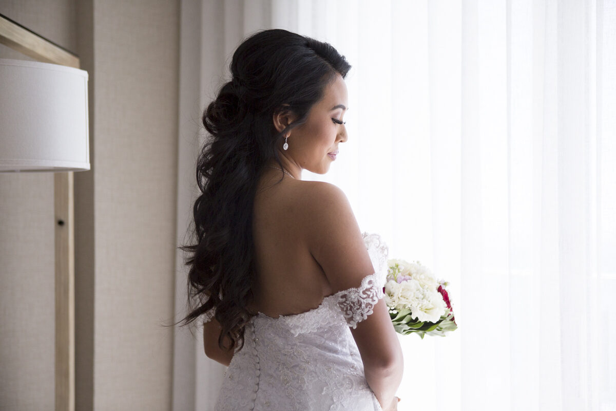 Bride in her dress by the window holding her bouquet, Hawaii wedding photography by Pure Media Hawaii